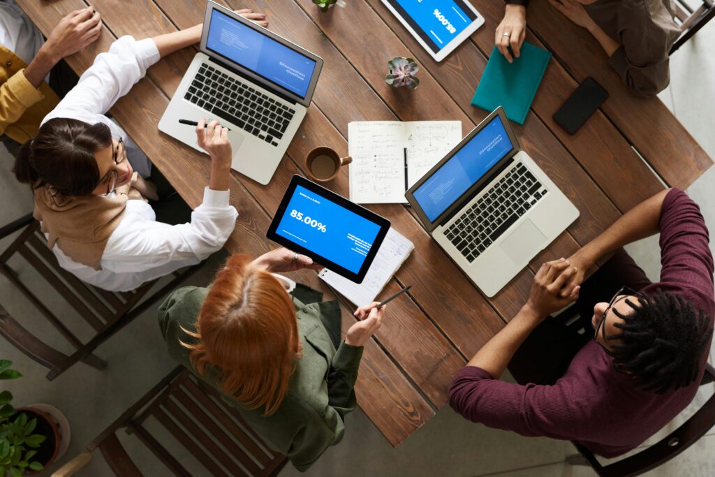 Diverse team discussing business strategies with laptops and tablets at a wooden table.