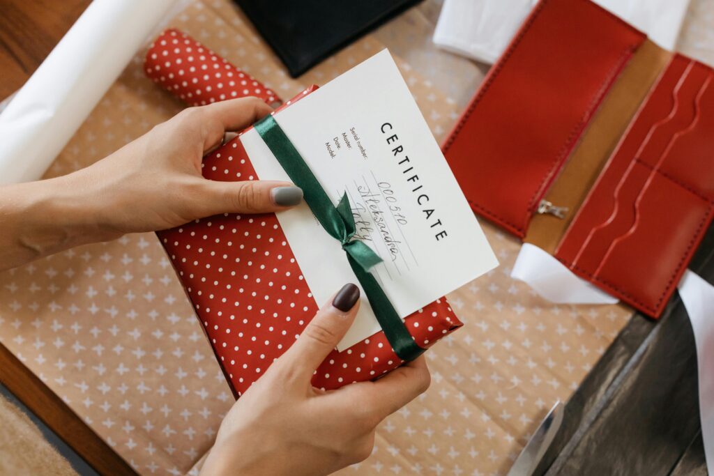 Close-up of hands holding a gift certificate wrapped in red polka dot paper and green ribbon.